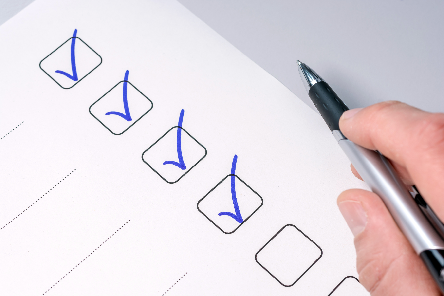 A hand holding a pen with four check boxes checked