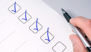 A hand holding a pen with four check boxes checked